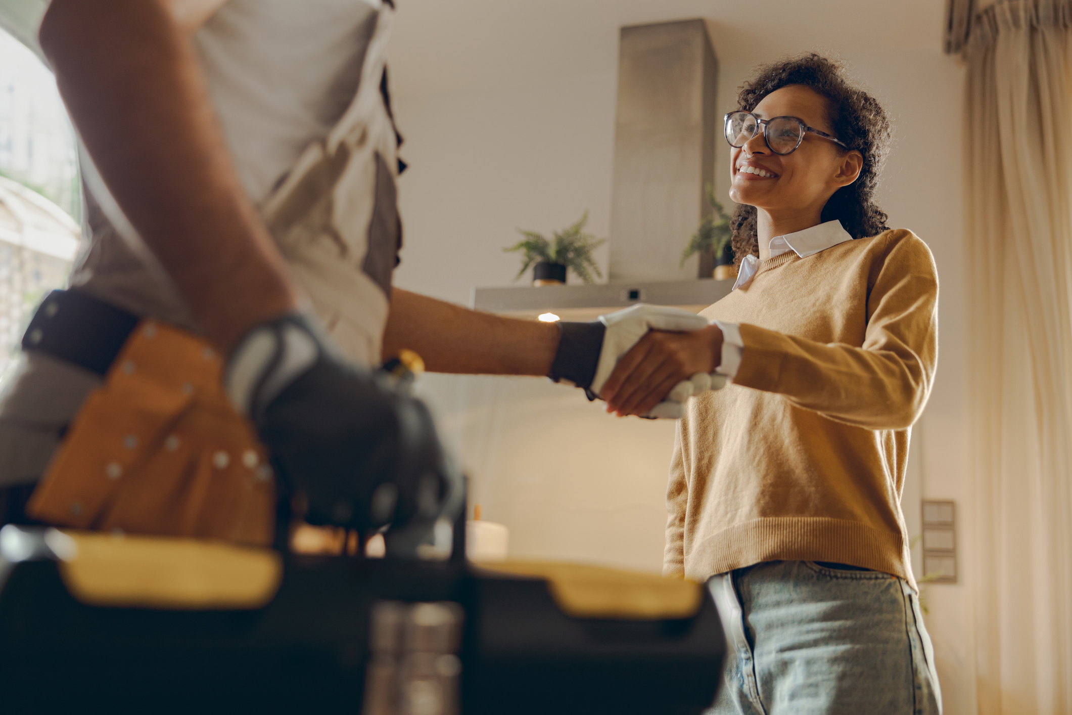 Close up of male handyman shaking hands with happy female client while standing at home kitchen0