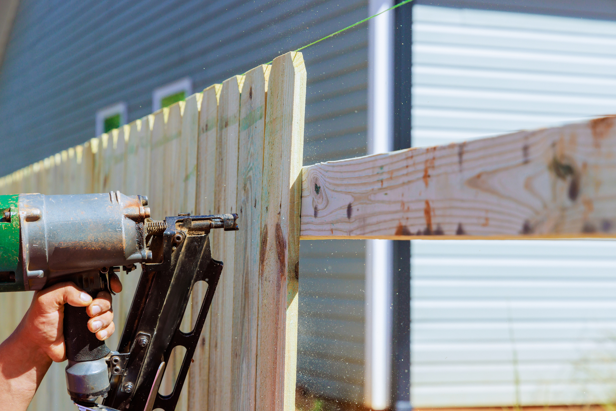 Man builds sections of nailing a wooden fence around his yard out planks